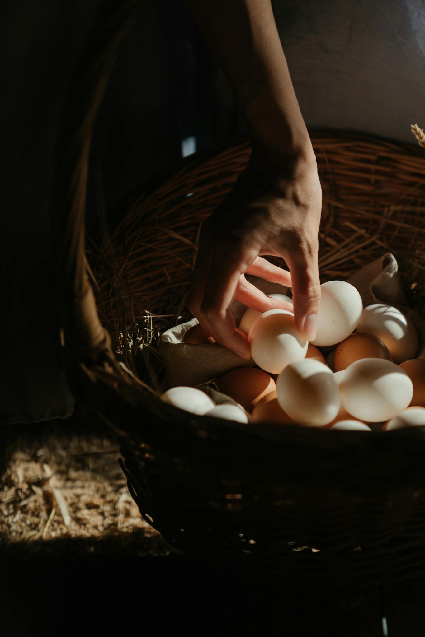 Hand collecting eggs from a wicker basket on a rustic farm setting.